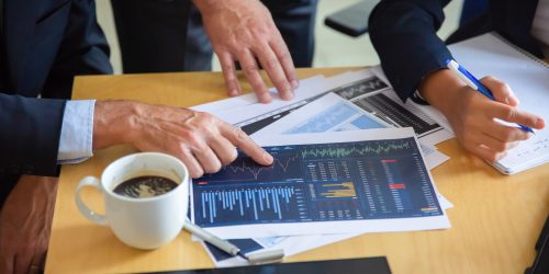 Unrecognizable businessman pointing at printed chart and showing graph to colleagues. Professional content partners making notes for statistics. Cooperation, communication and partnership concept